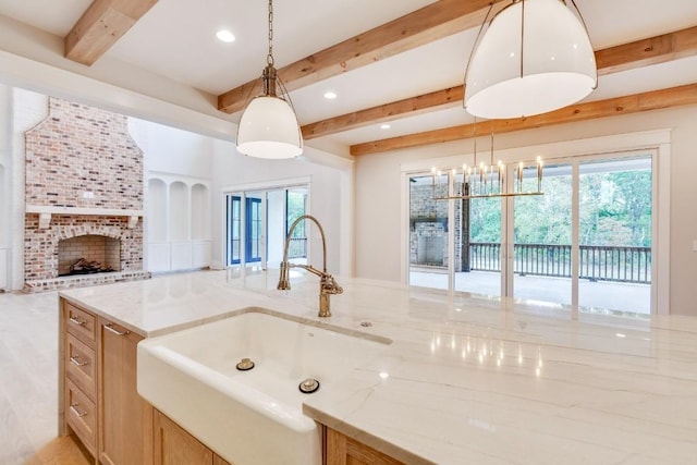 kitchen featuring beam ceiling, light stone counters, a healthy amount of sunlight, and a sink