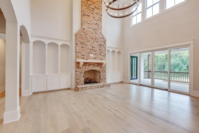 unfurnished living room with arched walkways, an inviting chandelier, wood finished floors, and a fireplace