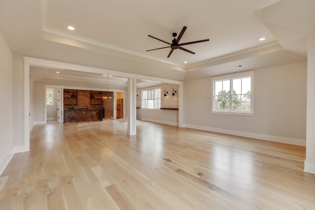 unfurnished living room with a wealth of natural light, a raised ceiling, and light wood-style floors