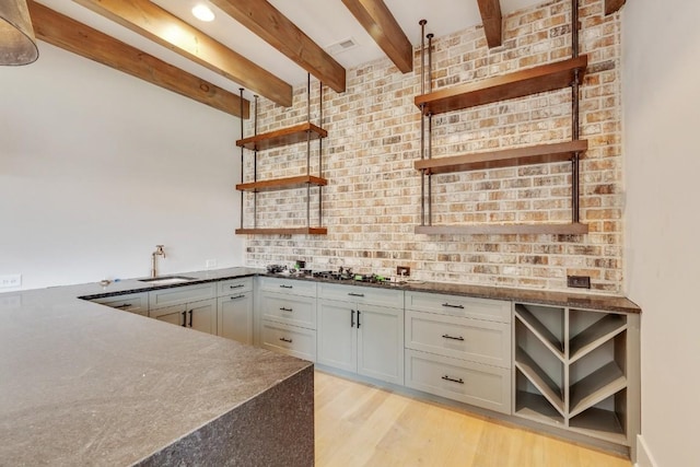 kitchen featuring visible vents, open shelves, beamed ceiling, light wood-style flooring, and a sink