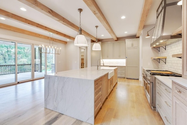 kitchen featuring light wood finished floors, high end stove, wall chimney range hood, beam ceiling, and a sink