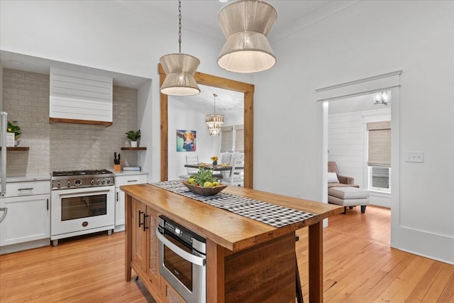 kitchen with gas range oven, tasteful backsplash, white cabinets, butcher block countertops, and light wood-type flooring