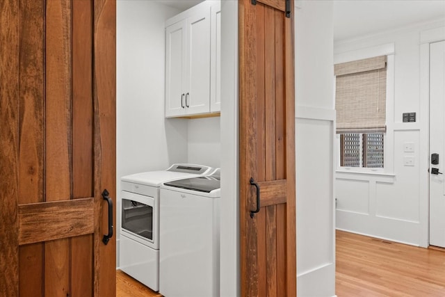 clothes washing area with light wood-style flooring, independent washer and dryer, and cabinet space