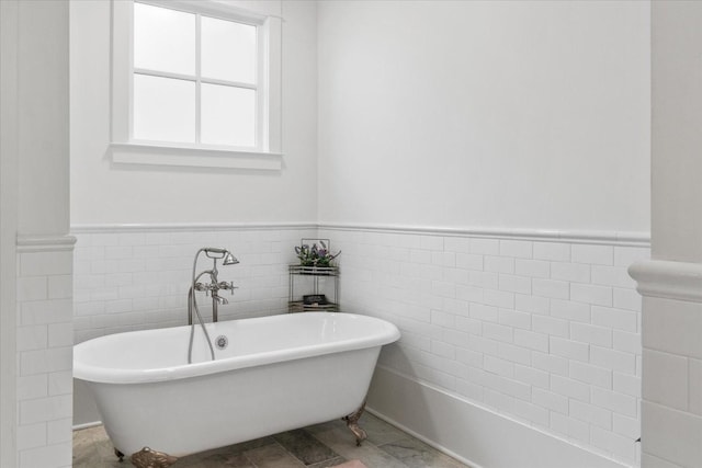 bathroom with a soaking tub, wainscoting, and tile walls