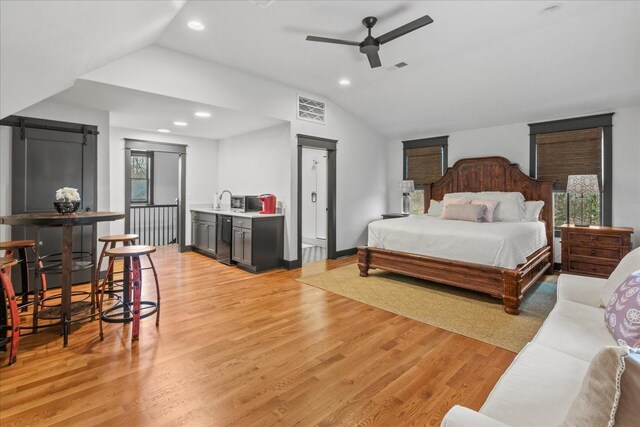 bedroom featuring vaulted ceiling, a barn door, visible vents, and light wood-style floors