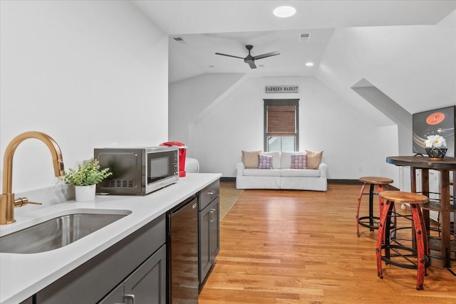 kitchen featuring light countertops, visible vents, vaulted ceiling, a sink, and light wood-type flooring