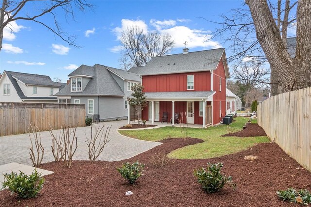 rear view of property featuring decorative driveway, a yard, central AC unit, board and batten siding, and fence