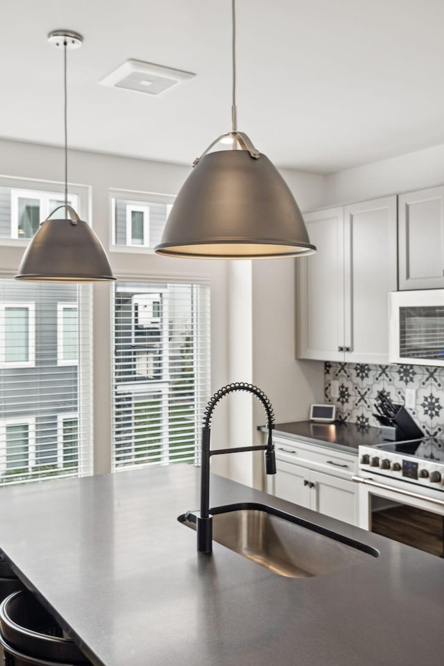 kitchen featuring white microwave, a sink, tasteful backsplash, dark countertops, and decorative light fixtures