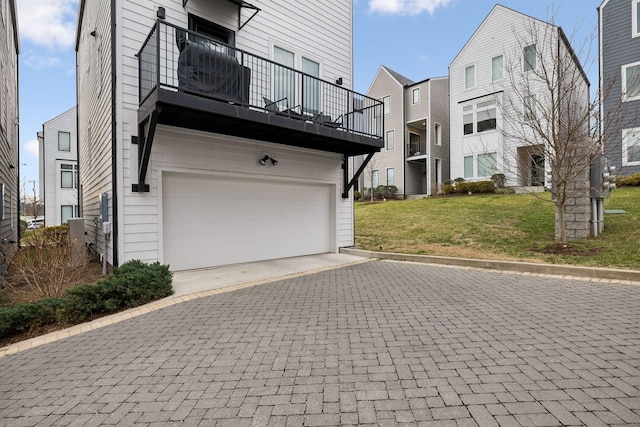 exterior space with a yard, an attached garage, a balcony, and driveway