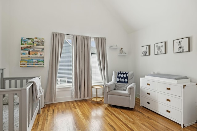 bedroom with light wood-style floors, vaulted ceiling, and a crib