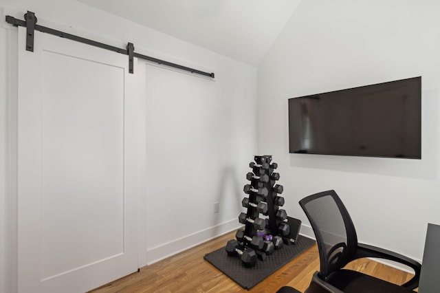 home office with wood finished floors, vaulted ceiling, baseboards, and a barn door