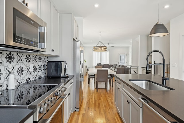 kitchen featuring stainless steel appliances, dark countertops, a sink, and light wood-style flooring