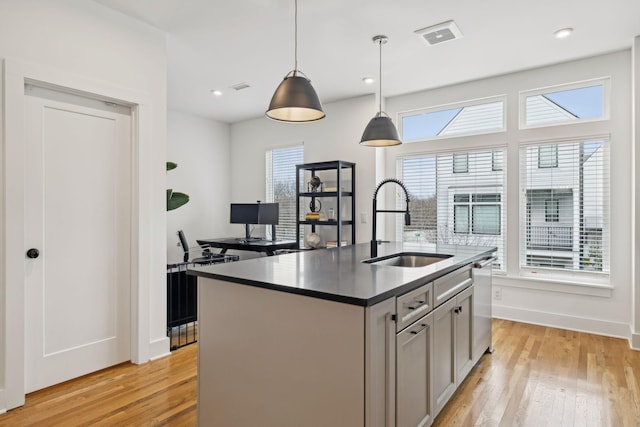 kitchen with dishwasher, a sink, a center island with sink, and light wood-style floors