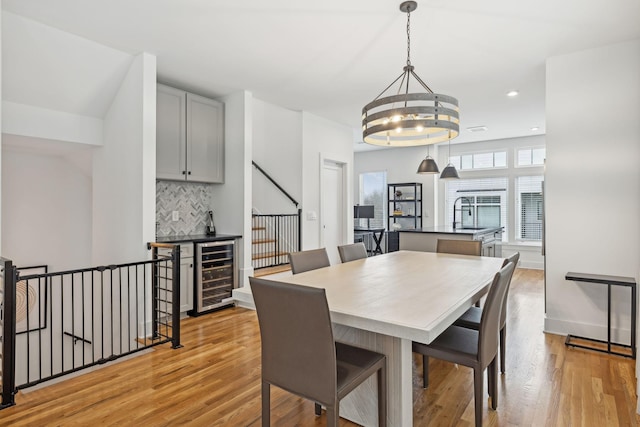 dining space with a notable chandelier, beverage cooler, recessed lighting, baseboards, and light wood-type flooring