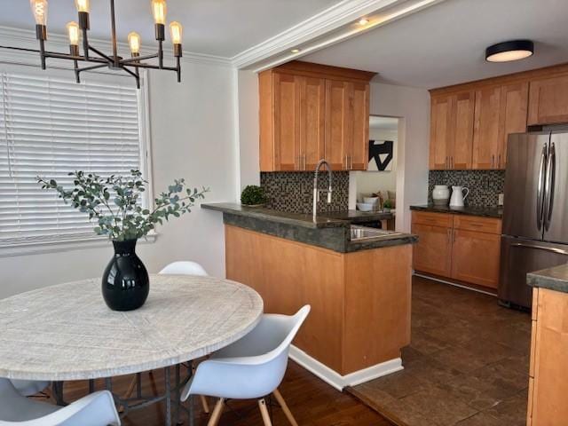 kitchen with brown cabinetry, a peninsula, freestanding refrigerator, ornamental molding, and dark countertops