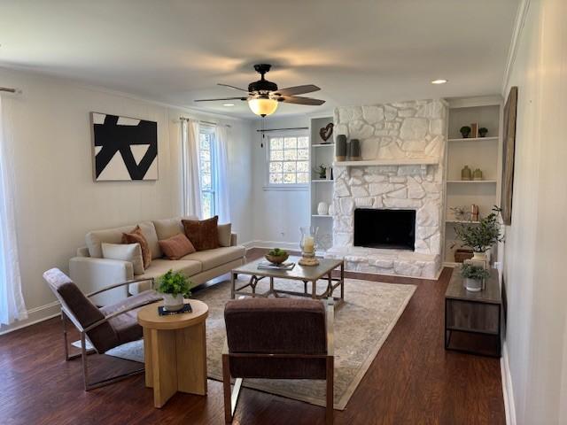 living area featuring baseboards, built in features, a fireplace, dark wood-style floors, and a ceiling fan