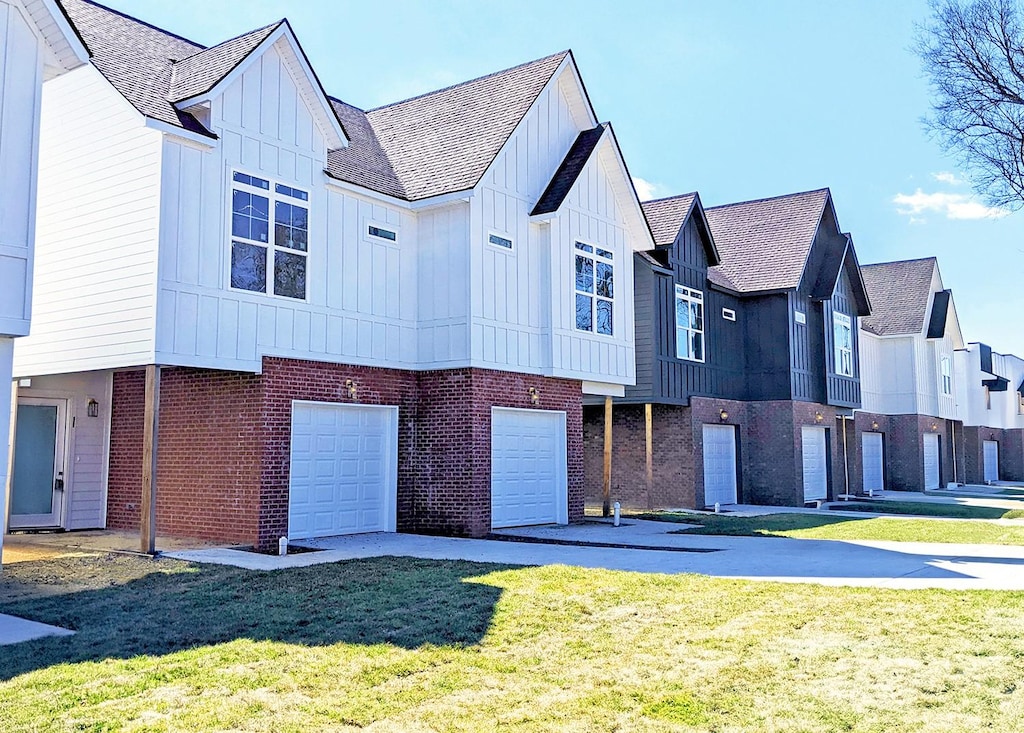 view of front facade featuring a garage, a front lawn, board and batten siding, and brick siding