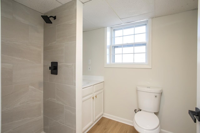 full bath with toilet, vanity, wood finished floors, tiled shower, and baseboards