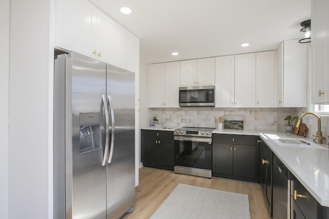 kitchen with light wood-style flooring, stainless steel appliances, light countertops, white cabinetry, and a sink