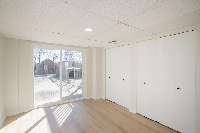 unfurnished bedroom with a paneled ceiling, access to exterior, light wood-style flooring, and multiple closets