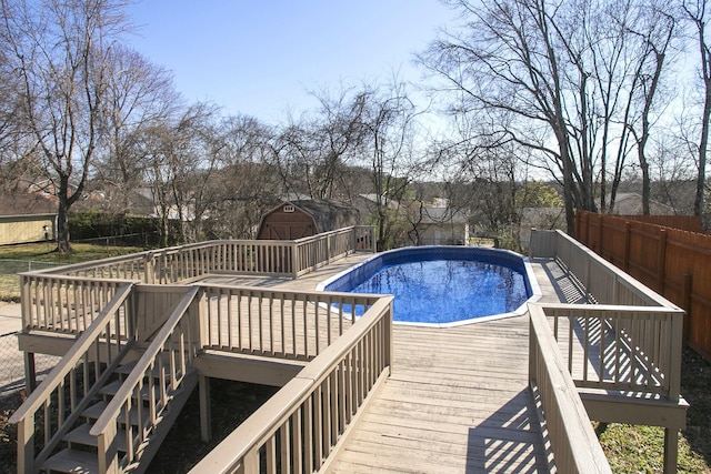 view of swimming pool featuring an outdoor structure, a wooden deck, a fenced in pool, and fence