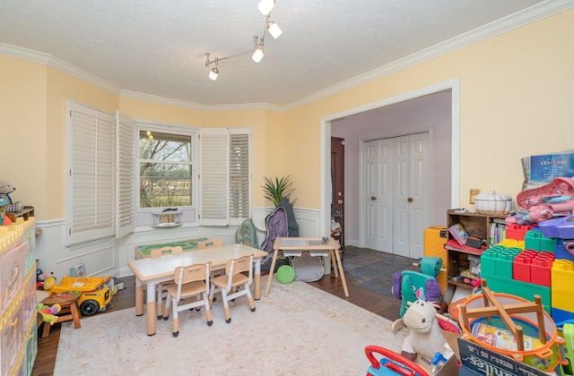 game room with a wainscoted wall, ornamental molding, a textured ceiling, and wood finished floors