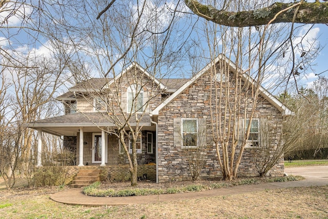 view of front of home with stone siding, covered porch, and roof with shingles