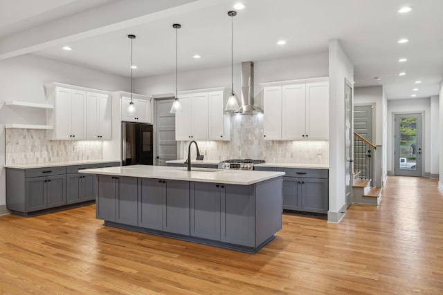 kitchen with wall chimney exhaust hood, black refrigerator, open shelves, and gray cabinetry