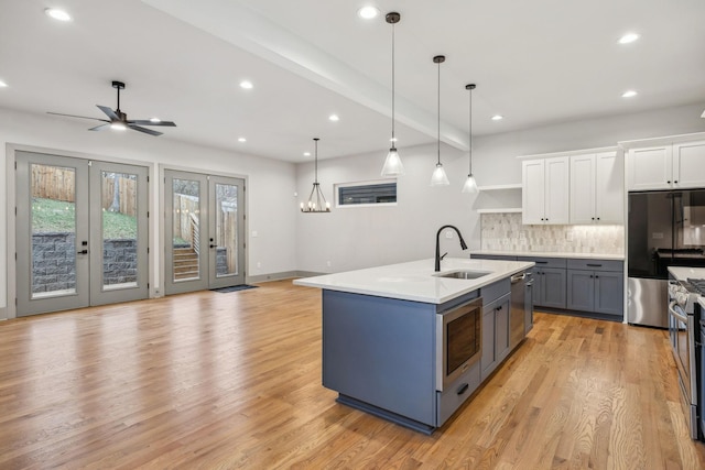 kitchen with french doors, light wood finished floors, appliances with stainless steel finishes, white cabinets, and a sink