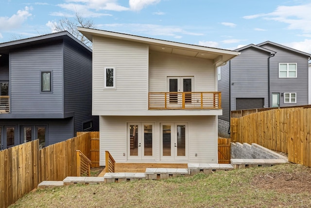 back of property with a balcony, a fenced backyard, and french doors