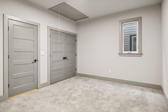 unfurnished bedroom with a closet, carpet flooring, attic access, and baseboards