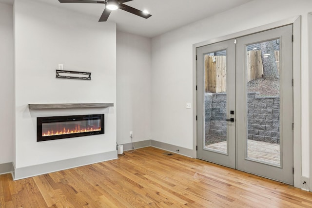 doorway featuring light wood finished floors, baseboards, a glass covered fireplace, ceiling fan, and french doors