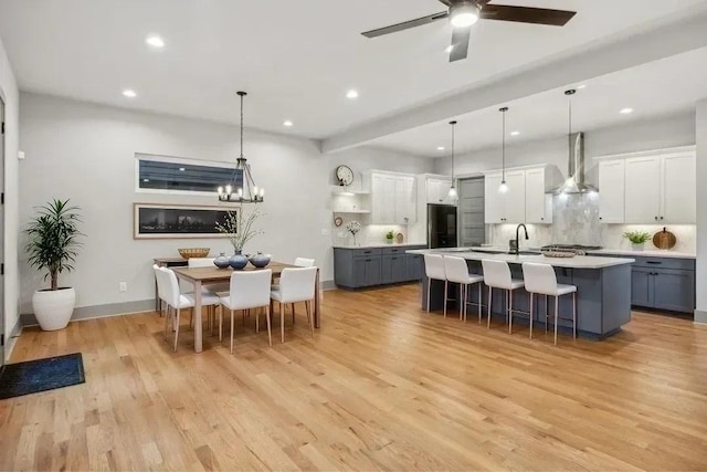 kitchen featuring refrigerator, open shelves, a kitchen breakfast bar, light countertops, and wall chimney exhaust hood