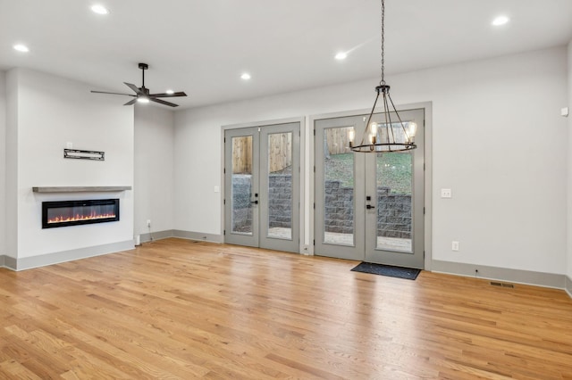 unfurnished living room with recessed lighting, baseboards, light wood-style floors, french doors, and a glass covered fireplace