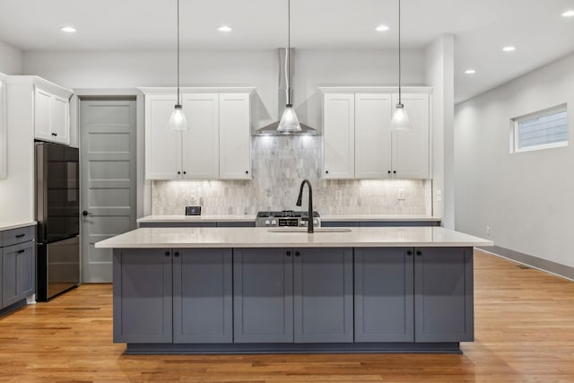 kitchen featuring an island with sink, a sink, freestanding refrigerator, and white cabinets