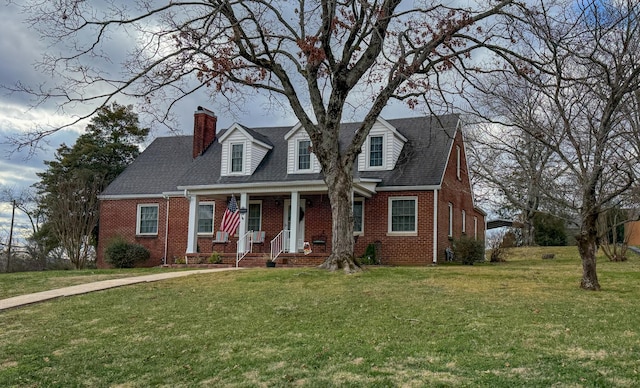 new england style home with a porch, a chimney, a front lawn, and brick siding