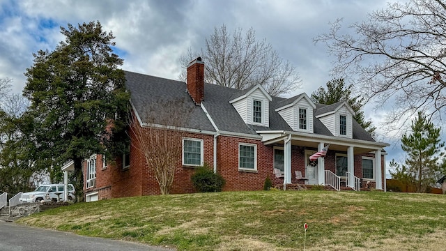 new england style home with roof with shingles, a front yard, a porch, and brick siding