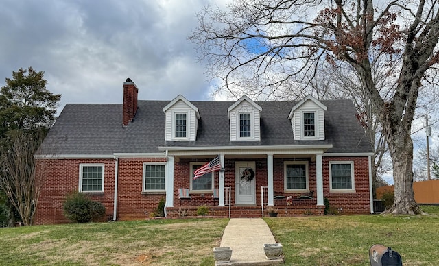 cape cod house featuring a chimney, brick siding, a front lawn, and a porch