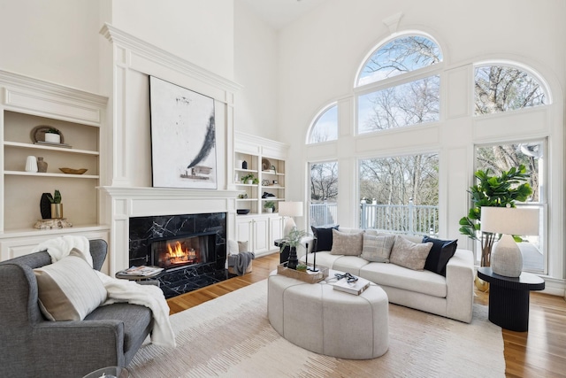 living room featuring a towering ceiling, built in shelves, wood finished floors, and a high end fireplace