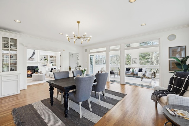 dining room featuring wood finished floors, a chandelier, a fireplace, and ornamental molding
