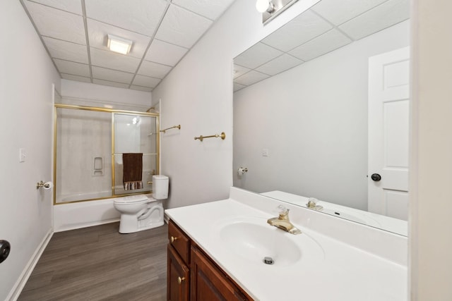 bathroom with toilet, a drop ceiling, wood finished floors, bath / shower combo with glass door, and vanity