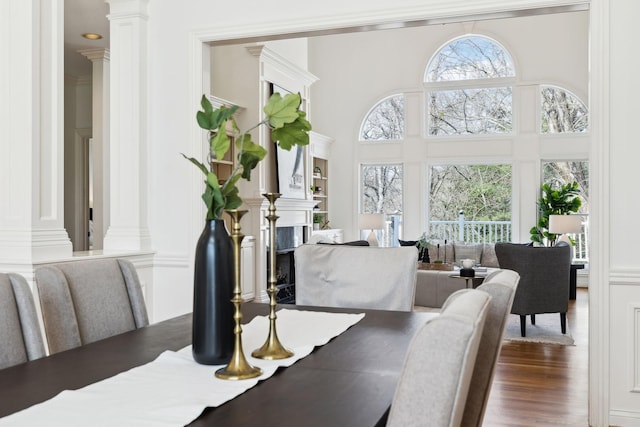 dining space featuring a towering ceiling, dark wood-style floors, ornate columns, and a premium fireplace
