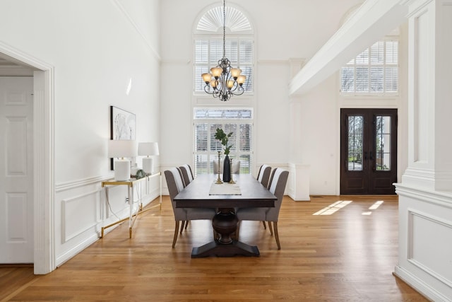 dining area featuring light wood-style floors, a high ceiling, a chandelier, and a decorative wall