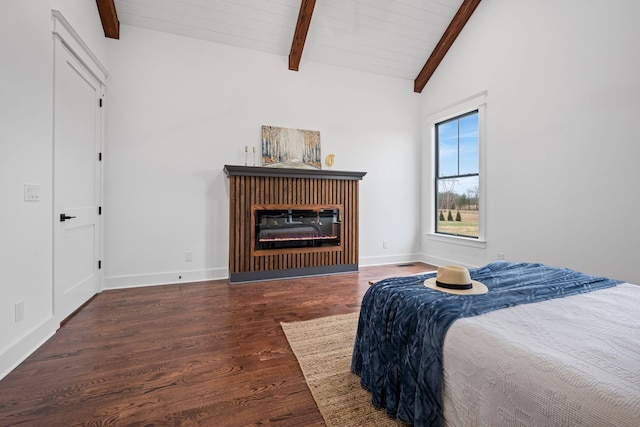 bedroom with vaulted ceiling with beams, a glass covered fireplace, wood finished floors, and baseboards