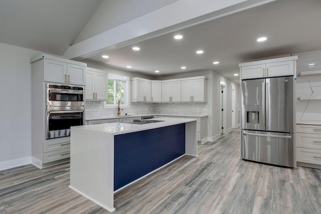 kitchen featuring a kitchen island, a sink, appliances with stainless steel finishes, backsplash, and light wood finished floors