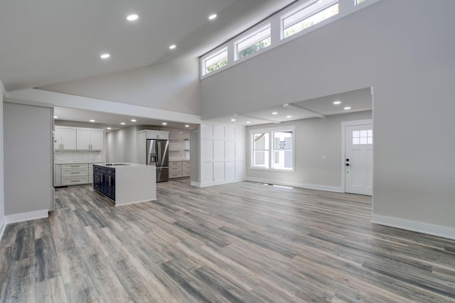 kitchen with open floor plan, high vaulted ceiling, stainless steel refrigerator with ice dispenser, and a kitchen island