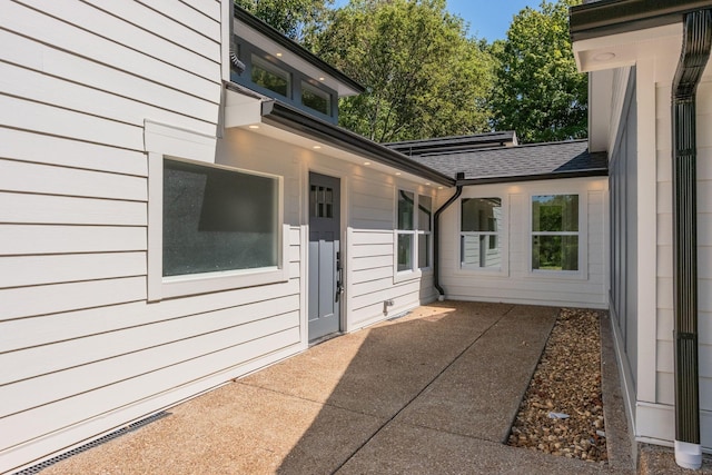 doorway to property with a patio area and roof with shingles