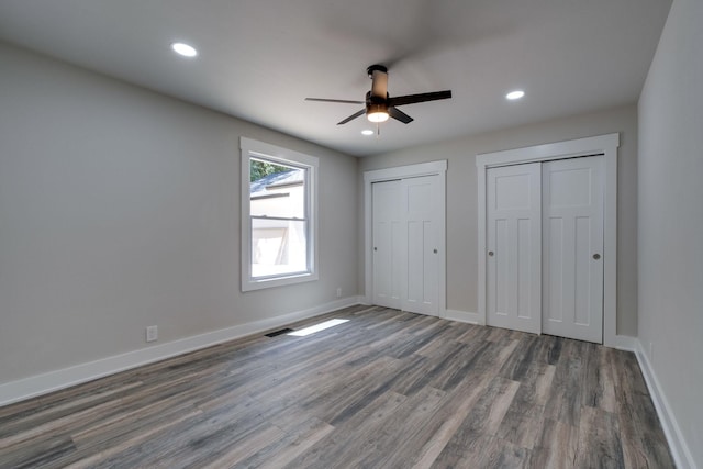 unfurnished bedroom featuring recessed lighting, wood finished floors, baseboards, and two closets