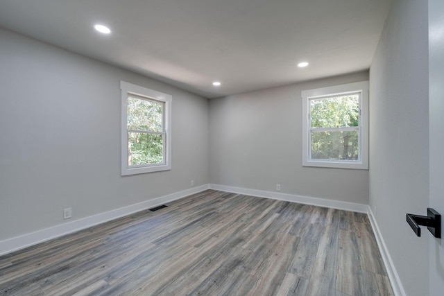 empty room with a wealth of natural light, wood finished floors, visible vents, and baseboards