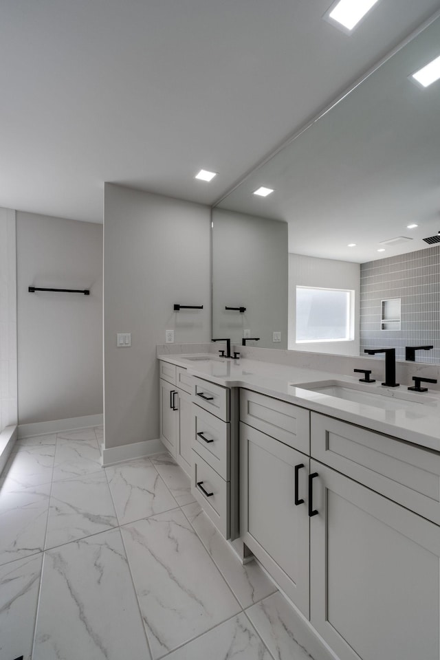 full bath with marble finish floor, a sink, baseboards, and double vanity